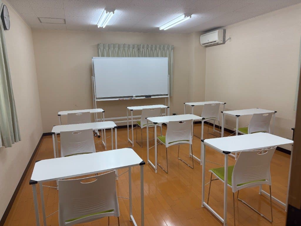 ホワイトボードと白い机が並ぶ、明るい教室